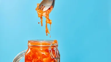 Un getto d'acqua si riversa in un bicchiere d'acqua trasparente pieno di erbe verdi e rosse e fette di barbabietola a strisce bianche e rosse.